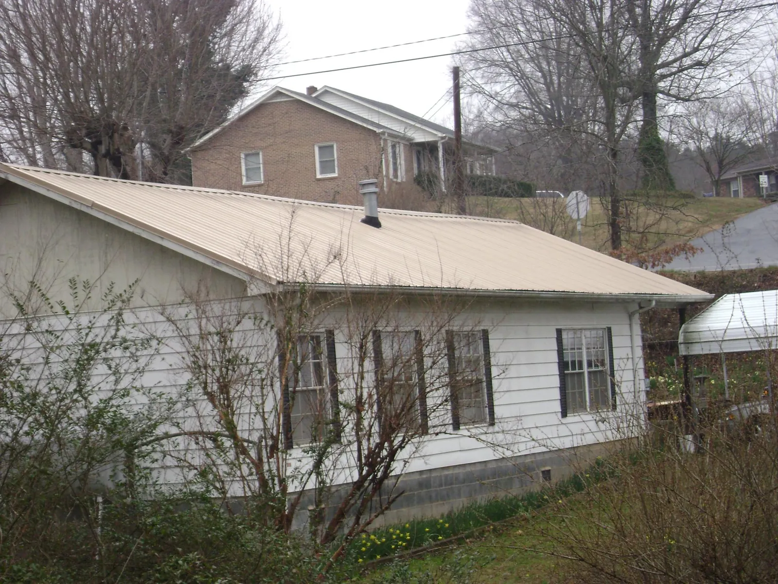 Tan metal roof on a white sided house set into a hillside — Commercial Roofing by Roofing Brothers in Eden